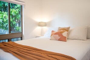 Ein Hotelzimmer mit einem Bett, einem Fenster mit Blick auf Grünflächen und einer Nachttischlampe.