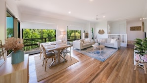 A spacious living area with a dining table, sofas, and a view of greenery. - Beach House on Main- Airlie Beach (Airlie Beach)