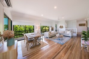 A spacious living area with a dining table, sofas, and a view of greenery. - Beach House on Main- Airlie Beach (Airlie Beach)
