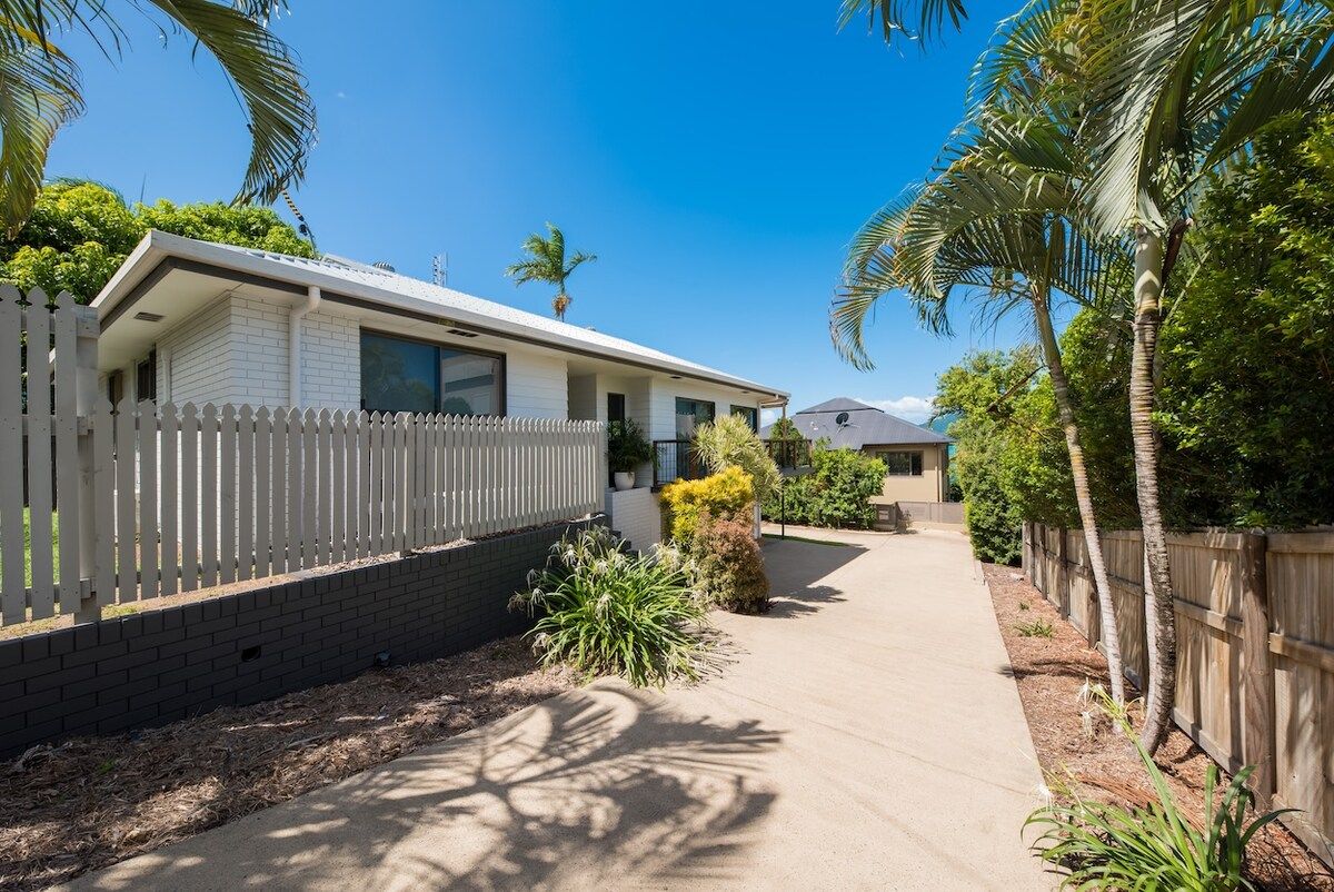 A single-story house with a white exterior, a picket fence, and a paved driveway.