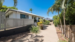 A single-story house with a white exterior, a picket fence, and a paved driveway. - Beach House on Main- Airlie Beach (Airlie Beach)