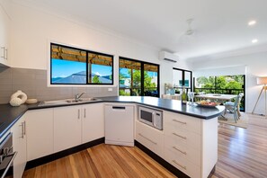A modern kitchen with white cabinetry, a built-in dishwasher, and a large island with a microwave. - Beach House on Main- Airlie Beach (Airlie Beach)