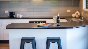 A modern kitchen with a central island, bar stools, and a bottle of champagne. - Beach House on Main- Airlie Beach (Airlie Beach)