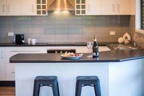 A modern kitchen with a central island, bar stools, and a bottle of champagne. - Beach House on Main- Airlie Beach (Airlie Beach)