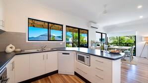 A modern kitchen with white cabinets, a black countertop, and a dishwasher. There are large windows with a view of greenery and a building.