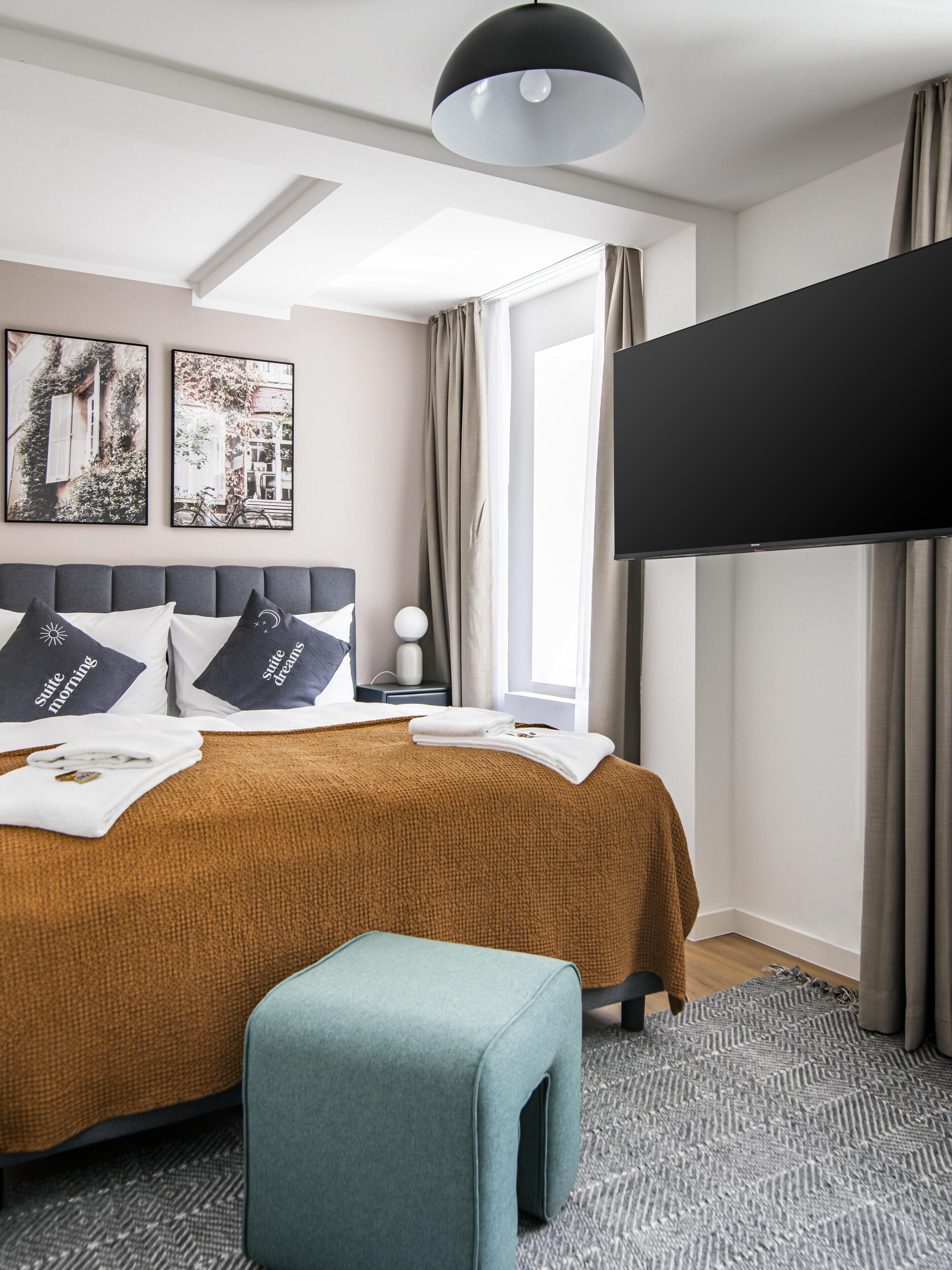 Une chambre d’hôtel moderne avec un grand lit, un téléviseur à écran plat, une petite table d’appoint et deux tableaux encadrés au mur.