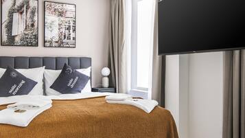 Une chambre d’hôtel moderne avec un grand lit, un téléviseur à écran plat, une petite table d’appoint et deux tableaux encadrés au mur.