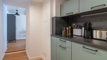 A modern kitchen with teal cabinets, a black countertop, and stainless steel appliances.