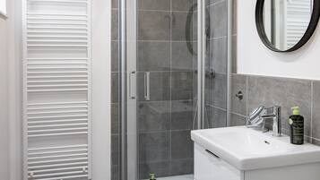 A modern bathroom with a glass-enclosed shower, a white sink with a mirror, and a wooden stool.