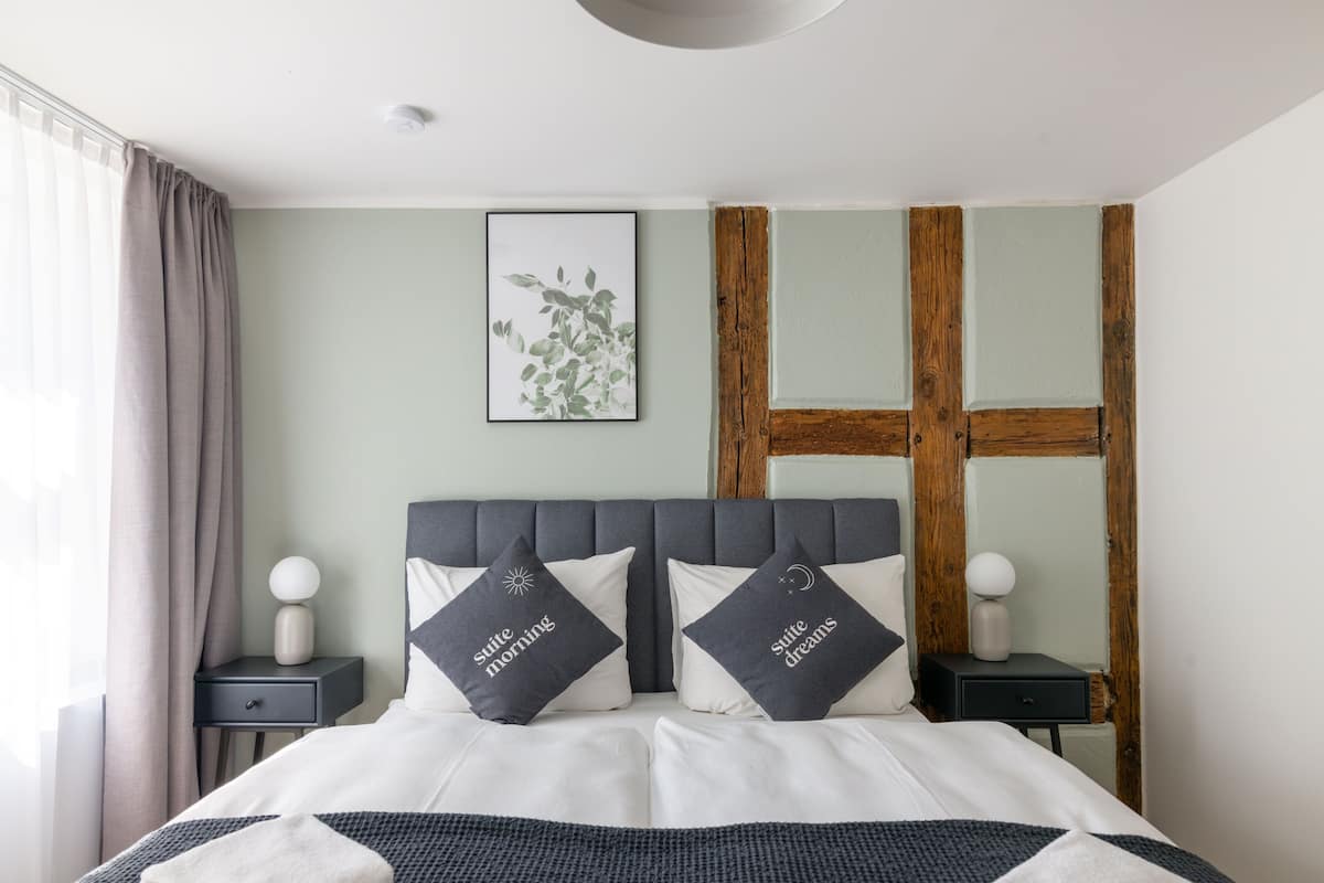 A neatly made bed with two pillows, a bedside table with a lamp, and a wall-mounted plant.