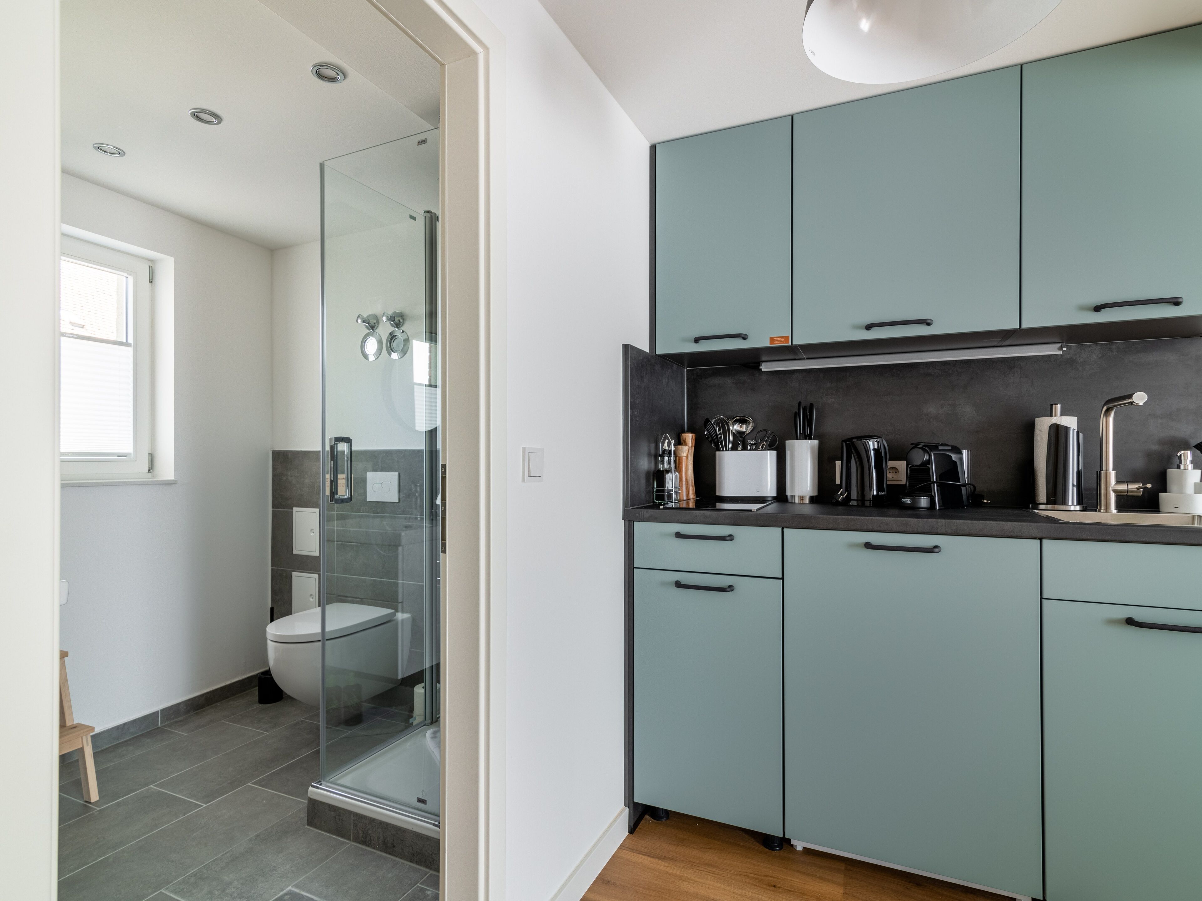 Une cuisine moderne avec des meubles de couleur turquoise, un plan de travail noir et une douche fermée par des parois de verre.