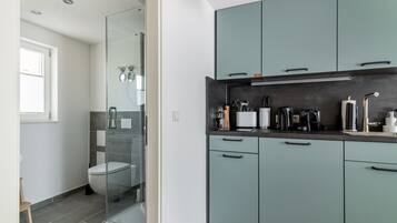 Une cuisine moderne avec des meubles de couleur turquoise, un plan de travail noir et une douche fermée par des parois de verre.