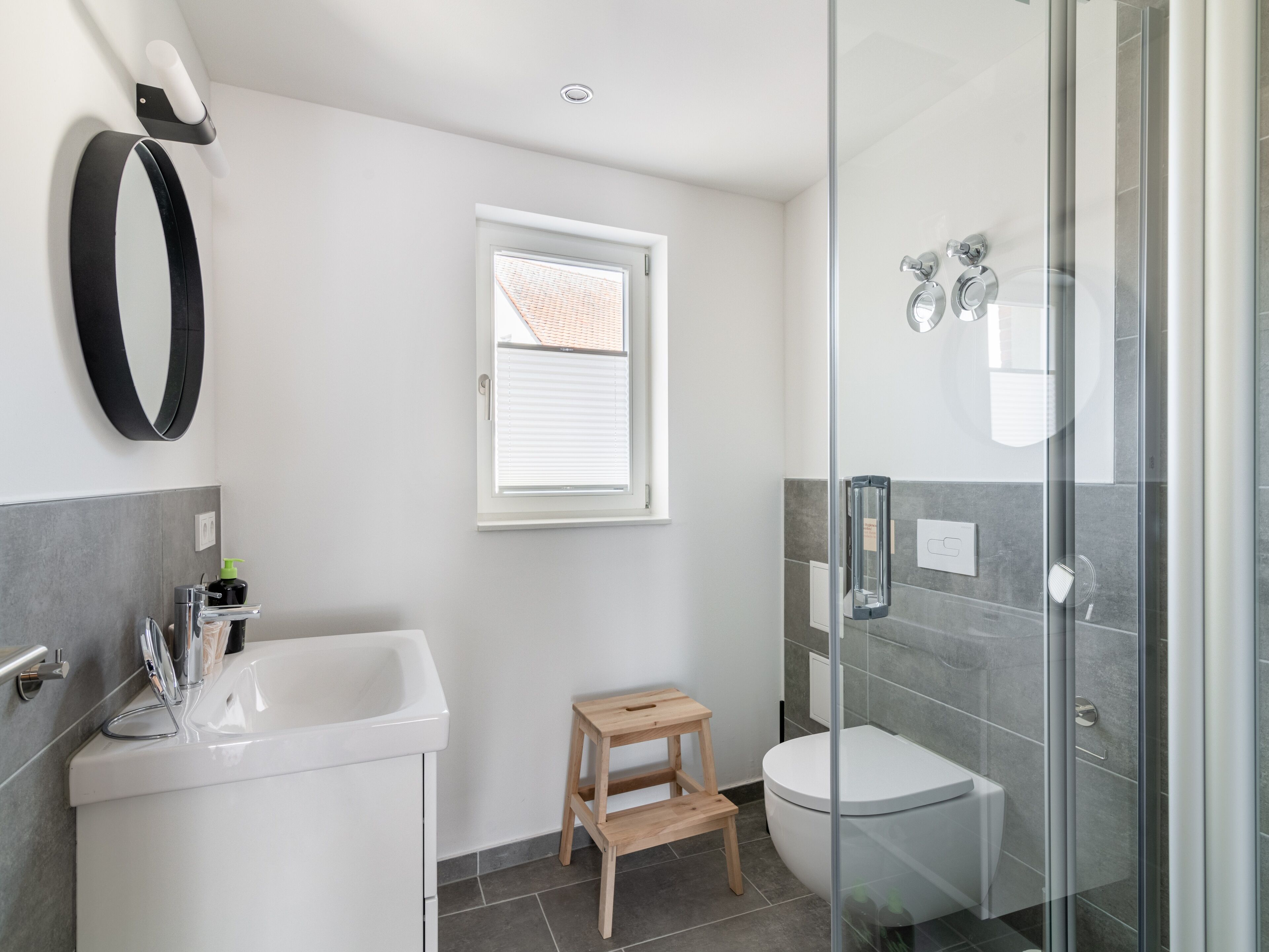 Une salle de bain moderne avec une douche à parois de verre, un lavabo blanc et un petit tabouret en bois.