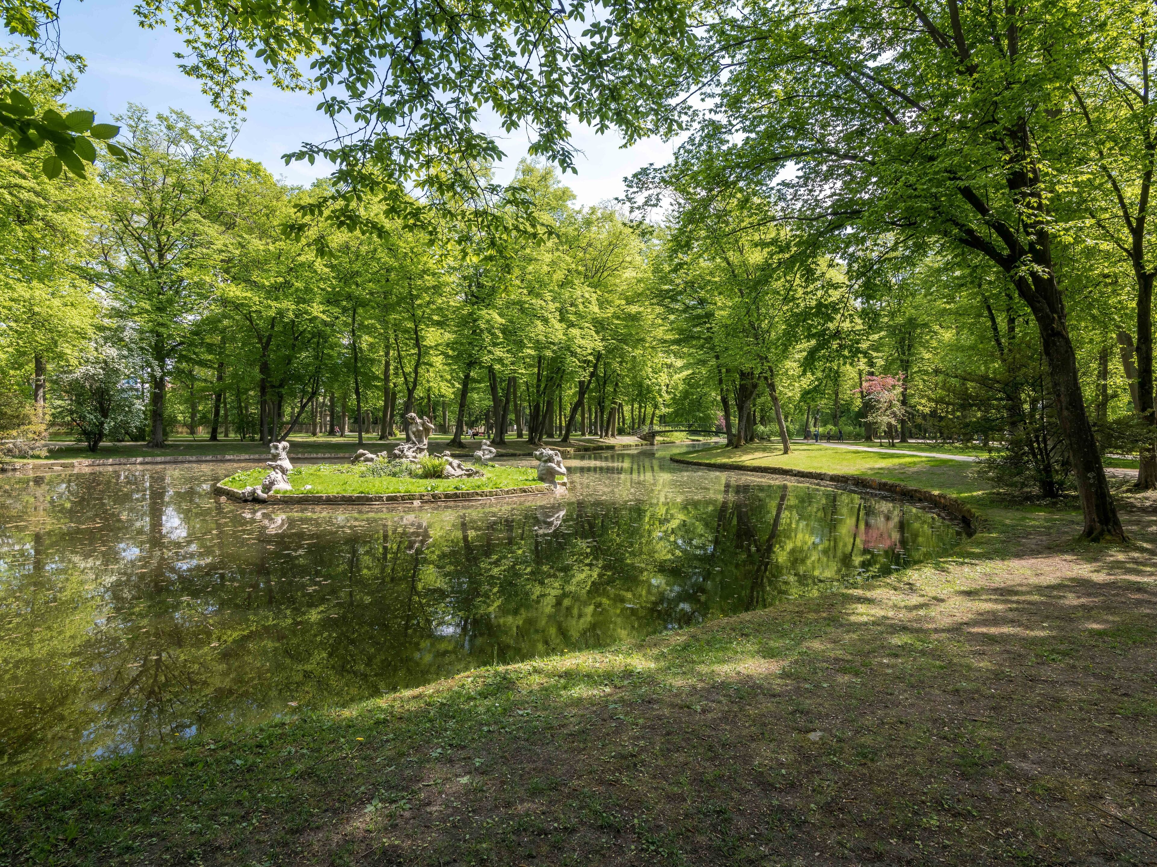 A serene park with a pond, surrounded by lush greenery and trees.
