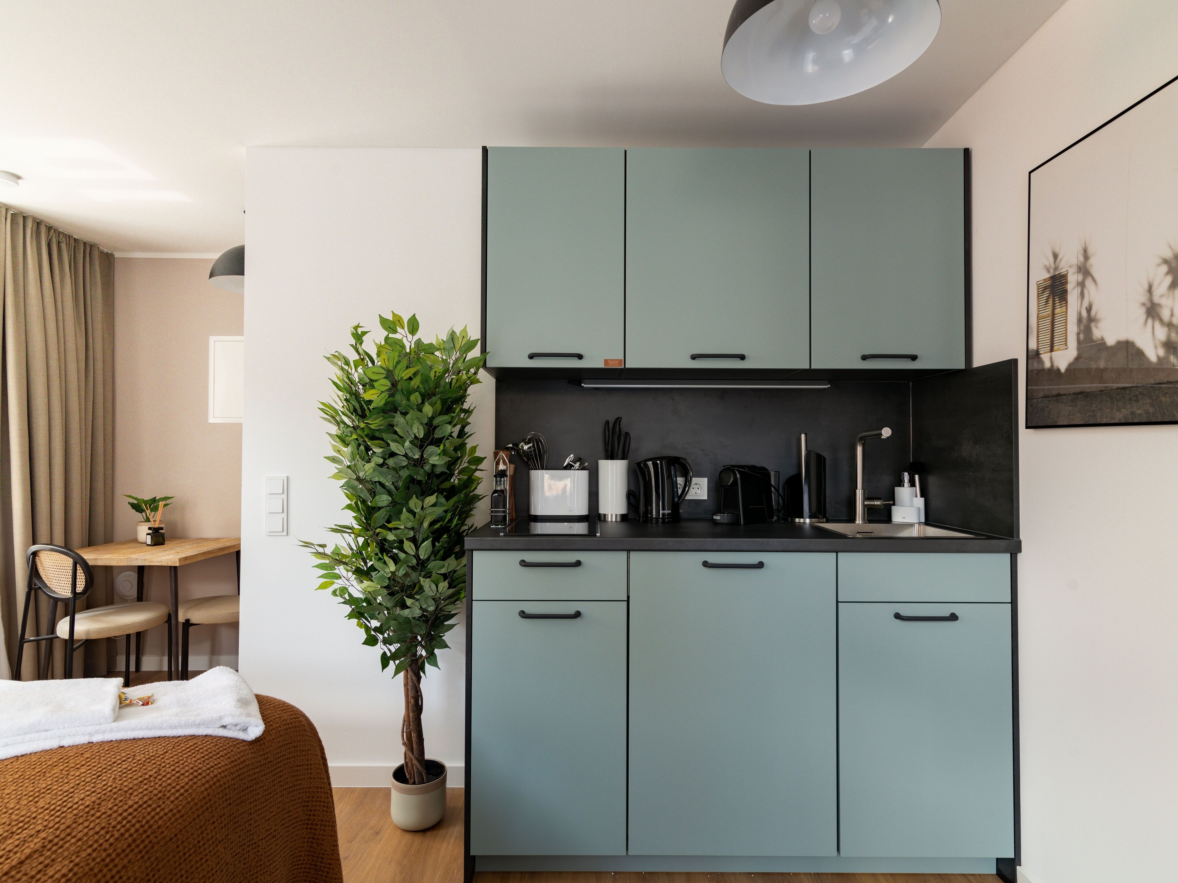 A compact kitchen with light blue cabinets, a coffee machine, and a potted plant.