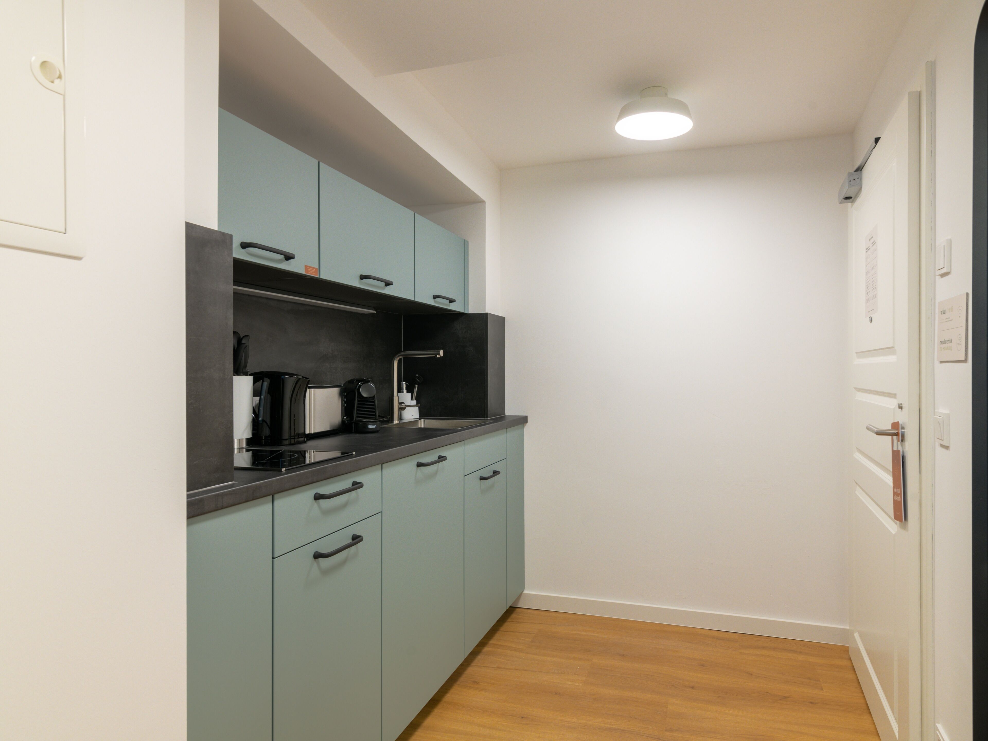 A compact kitchen with teal cabinets, a black countertop, and a single light fixture.