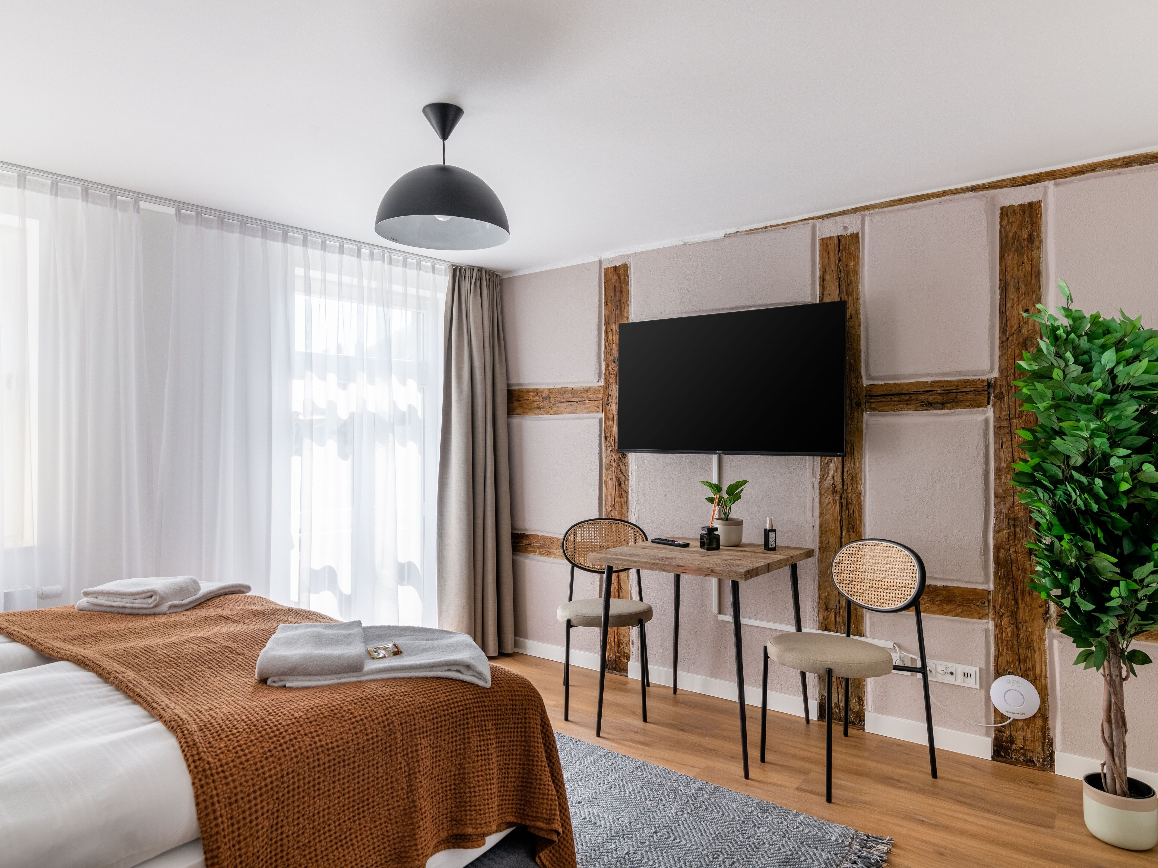 Une chambre d’hôtel moderne équipée d’un lit, d’un bureau, de deux chaises, d’une télévision et d’une plante en pot.