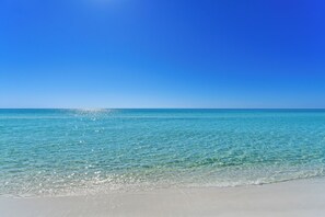 Une plage à l’eau turquoise et limpide, sous un ciel d’un bleu éclatant.
