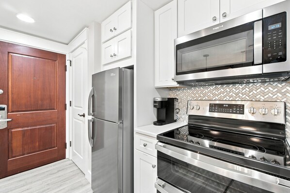A modern kitchen with stainless steel appliances, white cabinetry, and a herringbone tile backsplash.
