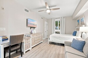 A hotel room with a bed, a desk with a chair, a television, and a ceiling fan.
