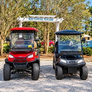 Two golf carts parked in front of a sign that reads 'Baytowne Wharf'.