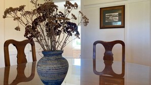 Une table à manger ornée d’un vase de fleurs séchées et accompagnée de deux chaises en bois.