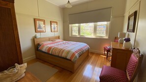 A bedroom with a wooden bed, a window with blinds, a wooden dresser, and a chair.