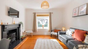 Ein Wohnzimmer mit Kamin, einer Couch, einem Fernseher und einem Fenster mit Vorhängen.