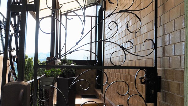 Un cancello in ferro battuto con decorazioni elaborate, un muro in mattoni e piante in vaso.