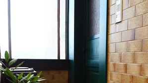 Un angolo di un edificio con una porta verde, una pianta in vaso e una finestra con persiane.