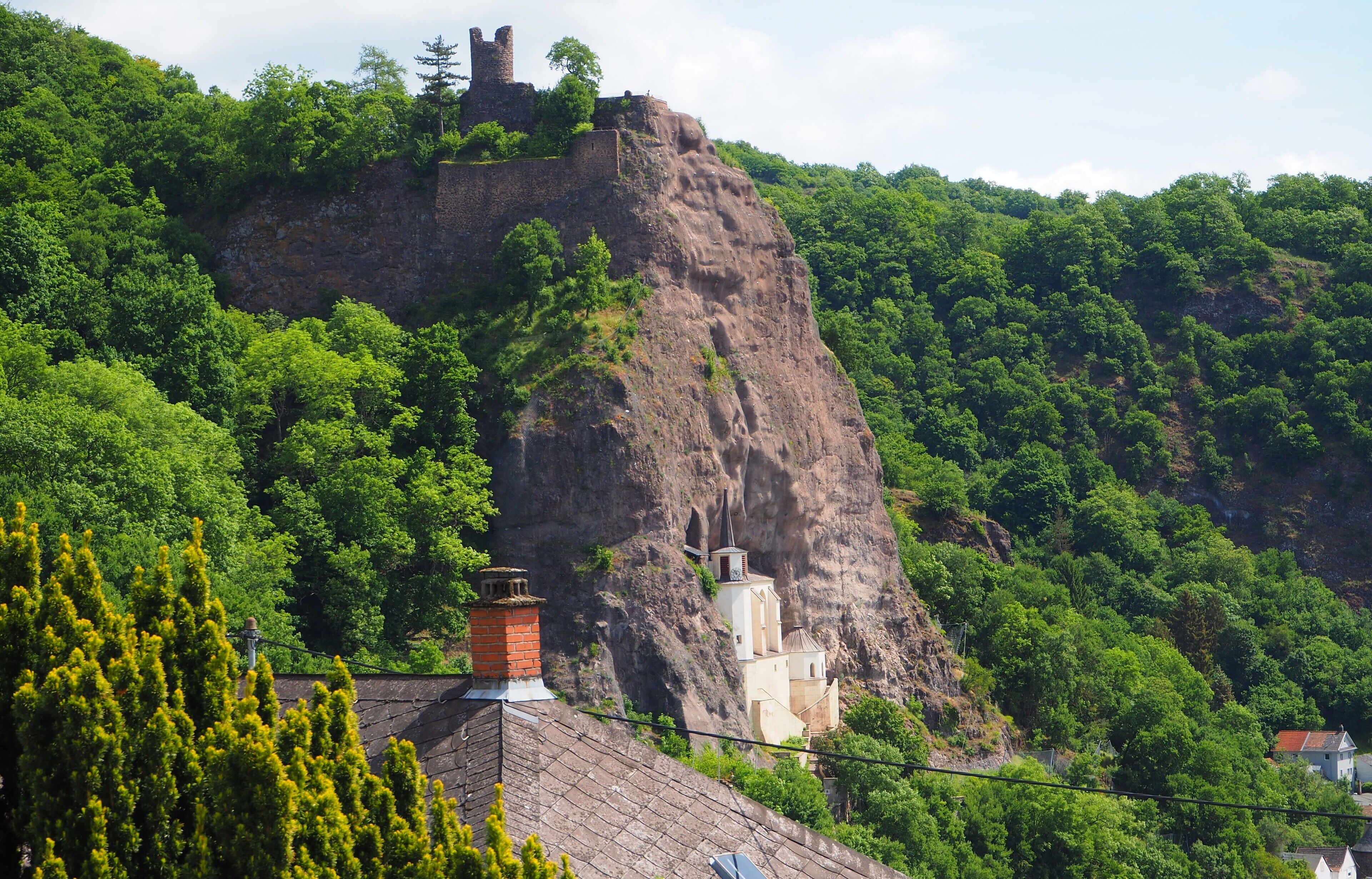 Eine Burg auf einem Hügel mit einer Kirche am Fuße, umgeben von dichtem Grün.