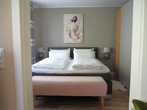 A neatly made bed with white linens, a headboard, and two bedside lamps.