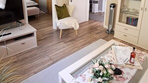 Un soggiorno moderno con una TV a schermo piatto, un divano, un tavolino da caffè con tovaglia floreale e un mobiletto con ante in vetro.
