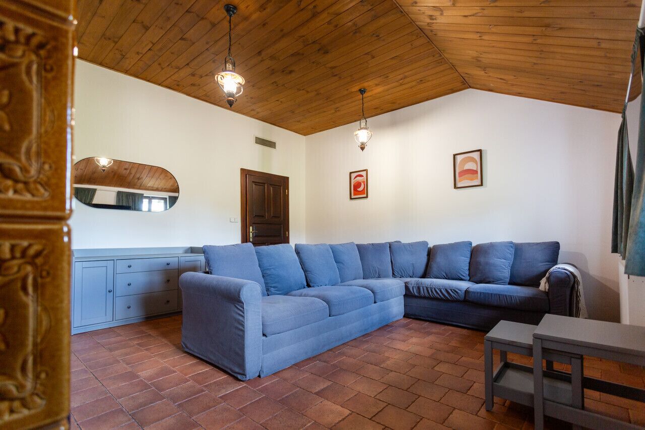 Un salon avec un canapé d’angle bleu, un plafond en bois et une petite table.
