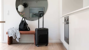 A room with a round mirror, a bench, a black suitcase, and a grey jacket on the bench.