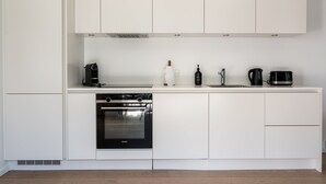 A modern kitchen with white cabinetry, a built-in oven, a coffee maker, and a kettle.