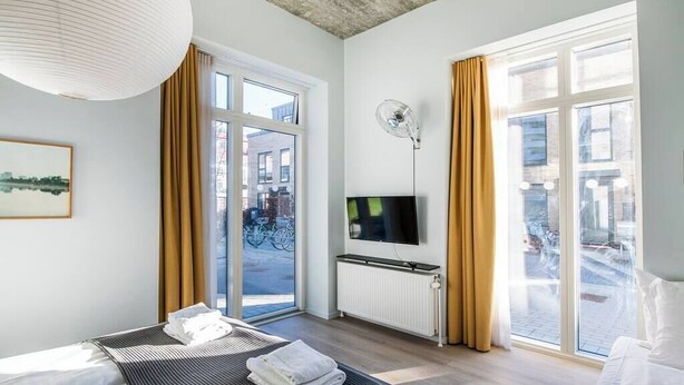 Une chambre d’hôtel moderne équipée d’un lit, d’un téléviseur à écran plat, d’une grande fenêtre et offrant une vue sur la rue.
