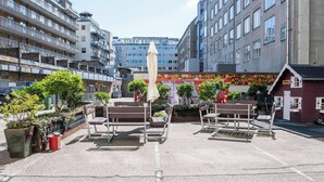 Ulkona on oleskelualue, jossa on penkkejä ja pöytä. Alue on koristeltu ruukkukasveilla ja värikkäällä seinämaalauksella.