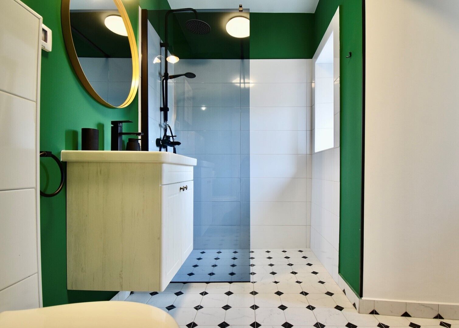 A bathroom with a white sink, green walls, a mirror, and a shower with a glass door.