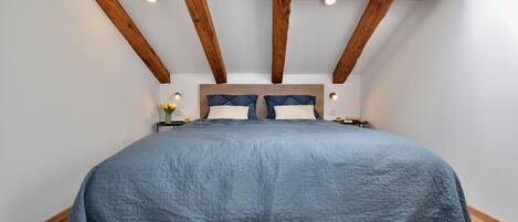 Un dormitorio con una cama grande, vigas de madera, un tragaluz y una mesita de noche con lámpara.