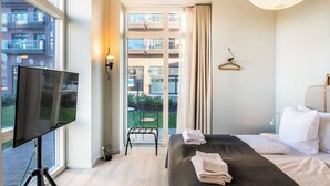 Ein Hotelzimmer mit Bett, Fernseher, Balkon mit Stuhl und Blick auf die umliegenden Gebäude.