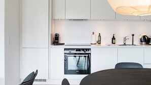 A modern kitchen with white cabinetry, a built-in oven, and a dining area with a table and chairs. - Beach gardens 2BR by Daniel & Jacob's (Copenhagen)