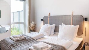 A modern hotel room with a large bed, two pillows, a bedside table, and a window with curtains. - Beach gardens 2BR by Daniel & Jacob's (Copenhagen)
