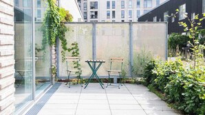 A courtyard with a glass wall, a metal fence, and a small table with chairs. - Beach gardens 2BR by Daniel & Jacob's (Copenhagen)