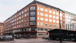 A multi-story building with a corner entrance, large windows, and a parking area with bicycles.