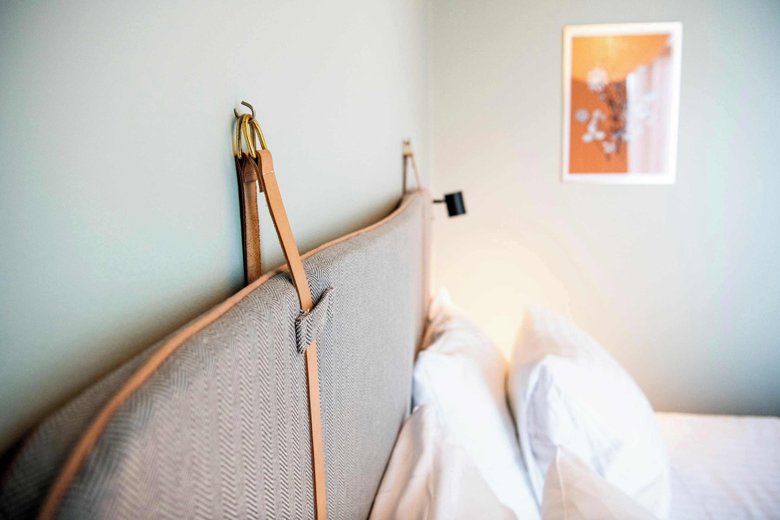 A bed with a headboard, a wall-mounted light switch, and a framed picture on the wall.