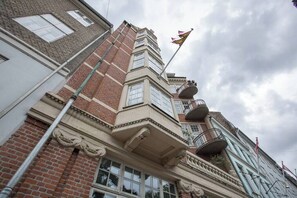Ein mehrstöckiges Gebäude mit einem markanten Balkon an der Ecke und einer Fahnenstange.