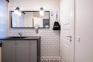 Ein Badezimmer mit weiß gefliesten Wänden, einem großen Spiegel mit Beleuchtung, einem Waschbecken und einer Tür mit Griff.