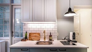 A kitchen with white cabinets, a stainless steel sink, a wooden cutting board, a bottle of olive oil, and a coffee machine. - The Citadel 2 by Daniel&Jacob's (København)