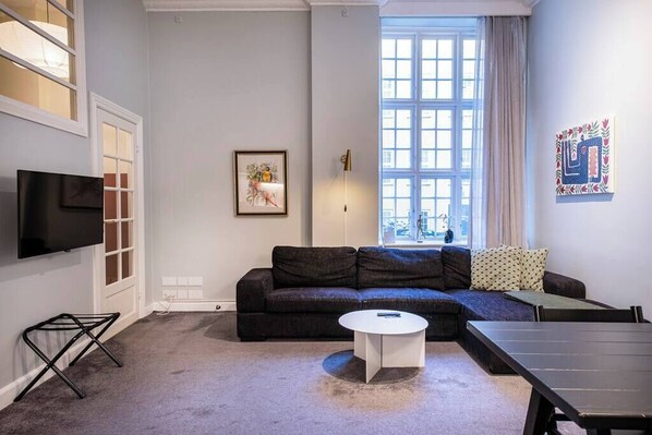 Ein modernes Wohnzimmer mit einem dunklen Sofa, einem weißen Couchtisch und einem an der Wand montierten Fernseher.